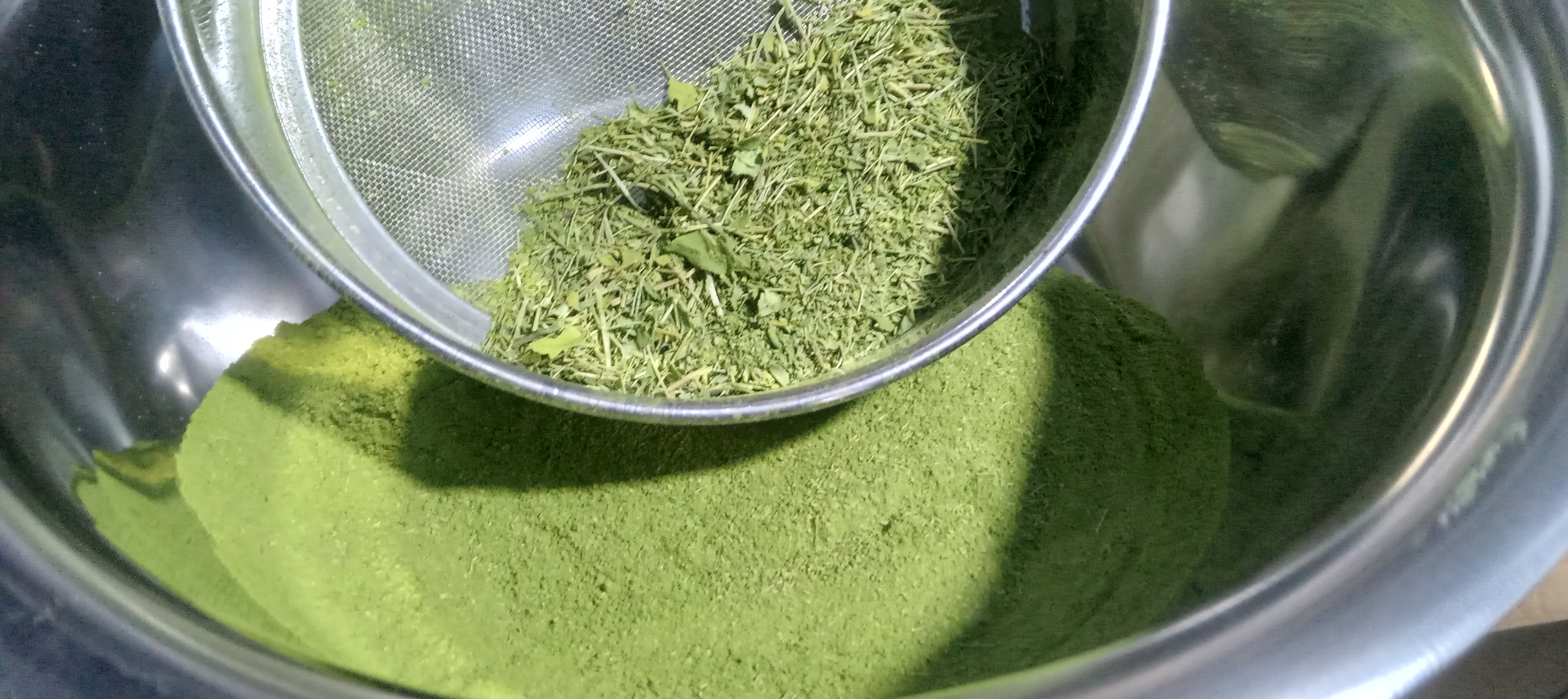 Fine moringa powder collected in a stainless-steel bowl with coarser particles retained in the sieve
